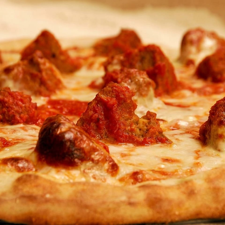 Close-up of a thick-crust pizza topped with meatballs, tomato sauce, and melted cheese.