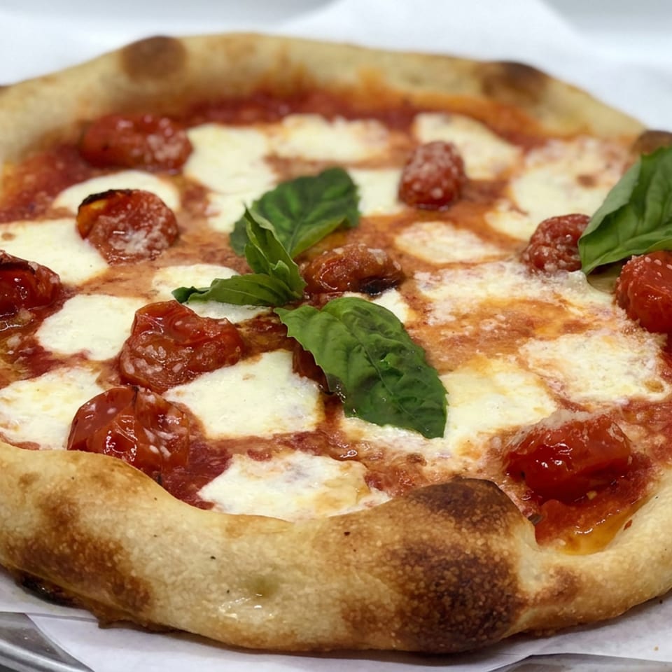 Neapolitan-style pizza topped with melted mozzarella, roasted tomatoes, tomato sauce, and fresh basil on parchment paper.