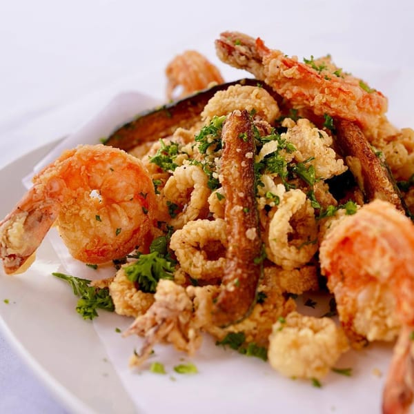 A white plate piled high with golden-fried calamari, shrimp, and zucchini, garnished with fresh parsley.