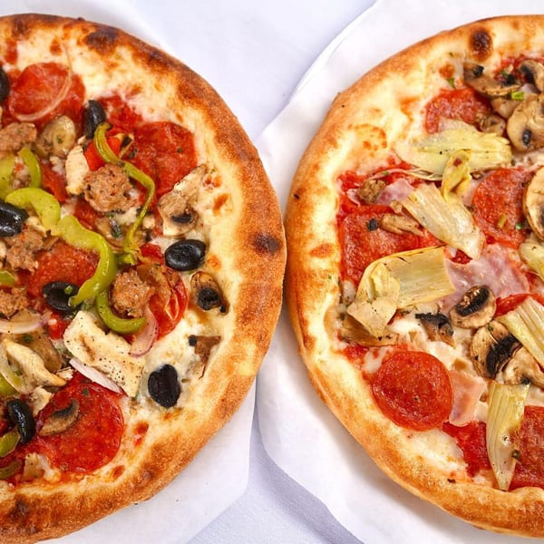 Two pizzas with various toppings, including pepperoni, mushrooms, olives, and peppers, on white paper.