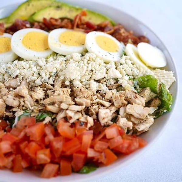 A vibrant Cobb salad with avocado, bacon, hard-boiled eggs, blue cheese, chicken, and tomatoes.