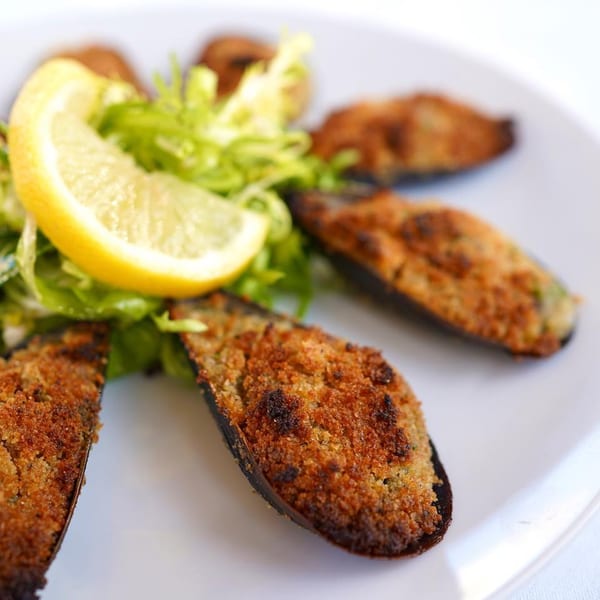 Baked mussels with crispy breading, served with a lemon wedge and green salad on a white plate.